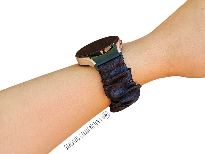 May include: A black silicone watch band with a scrunchie-like design. The band is worn on a silver Samsung Galaxy Watch 4.