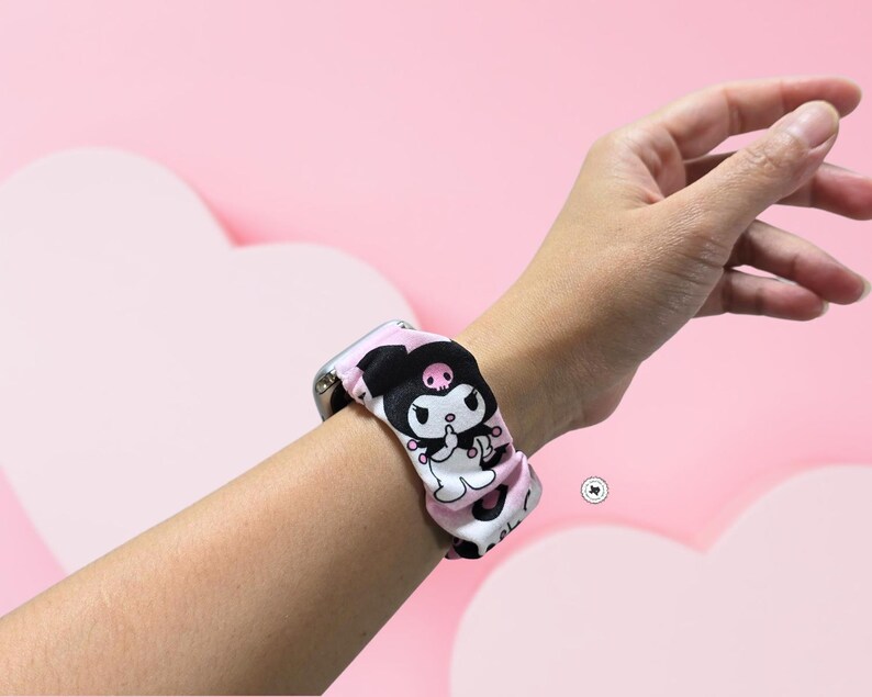 Op de afbeelding: Een patroon horlogebandje in zwart, wit en roze, met een cartoon karakter ontwerp. De band is bevestigd aan een zilveren horloge en wordt om de pols gedragen. De achtergrond is lichtroze.