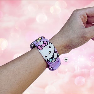 May include: A purple and white watch band with a Hello Kitty design. The band is made of fabric and has a soft, comfortable feel.