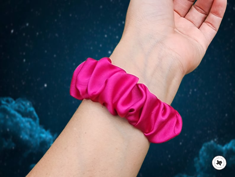 May include: A bright pink satin scrunchie, worn on a person's wrist.