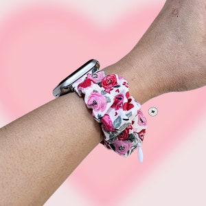 Peut inclure: Bracelet de montre scrunchie floral avec un cadran argent&eacute;. Le scrunchie pr&eacute;sente un fond blanc avec des roses rouges et roses et des feuilles vertes. Une petite fermeture &eacute;clair blanche est visible sur le c&ocirc;t&eacute;.