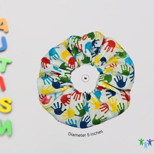 Puede incluir: Un scrunchie blanco con huellas de manos de colores. El scrunchie tiene un di&aacute;metro de 5 pulgadas.
