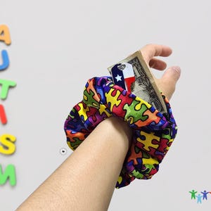 May include: A colorful wristband with a puzzle piece pattern. The wristband is worn on a person's wrist and has a small Texas flag sticker and a dollar bill tucked into it.