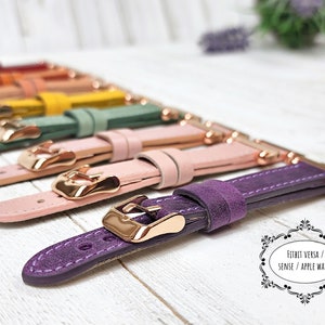 May include: A selection of watch straps in a range of colours, such as purple, pink, green, and yellow. Each strap has a gold-coloured buckle and connector. The straps are designed for Fitbit Versa, Sense, and Apple Watch.
