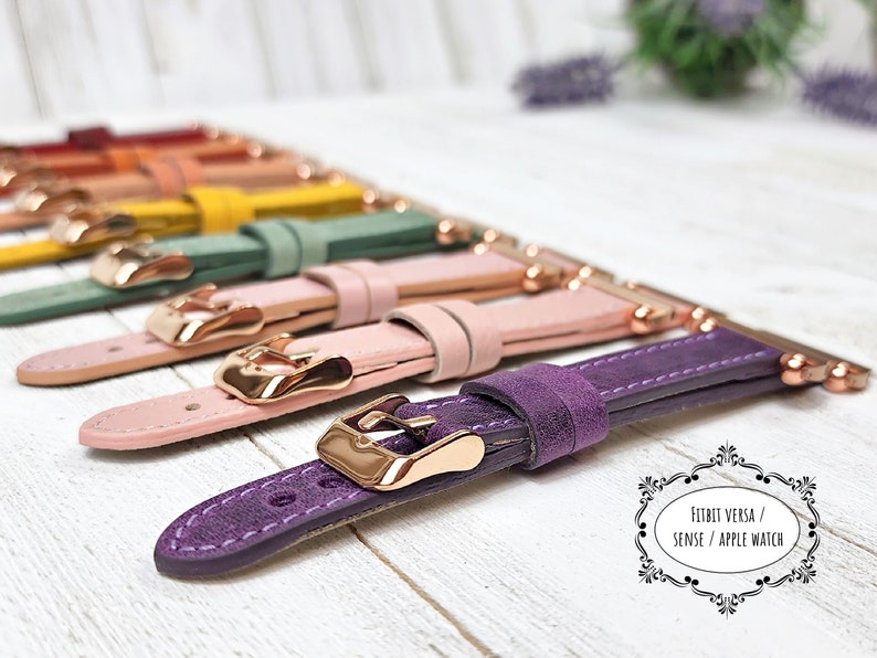 May include: A selection of watch straps in a range of colours, such as purple, pink, green, and yellow. Each strap has a gold-coloured buckle and connector. The straps are designed for Fitbit Versa, Sense, and Apple Watch.