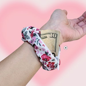 Peut inclure: Un portefeuille de poignet &agrave; imprim&eacute; floral avec une fermeture &eacute;clair blanche, contenant un billet de dix dollars. Le tissu pr&eacute;sente un motif de roses rouges et roses sur fond blanc. Le bracelet est con&ccedil;u pour &ecirc;tre port&eacute; autour du poignet.