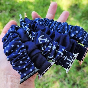Peut inclure: Bracelets de montre scrunchie bleu marine avec des motifs de pois blancs, d'ancres et d'étoiles. Les bracelets sont tenus dans une main, présentant les différents motifs et le matériel de fixation de la montre.
