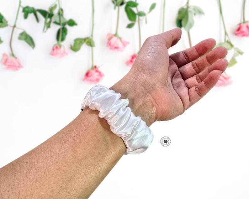 May include: White satin scrunchie worn on a wrist as a bracelet.