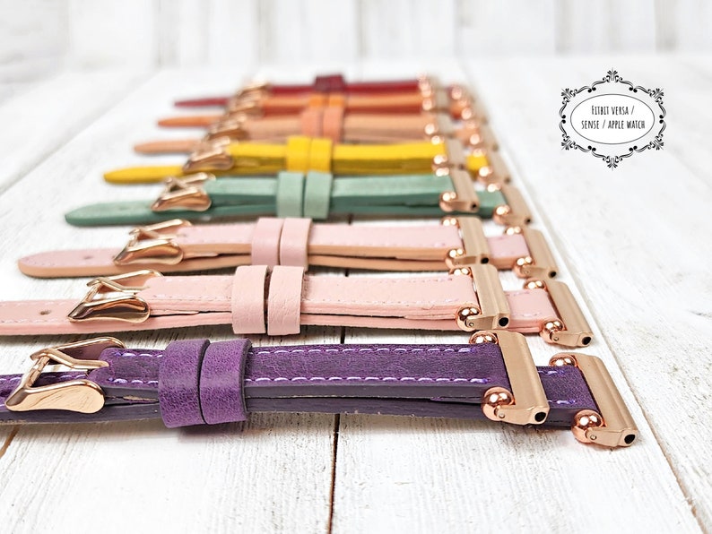 May include: A selection of colourful leather watch straps in shades like purple, pink, green, and yellow. Each strap has a rose gold buckle and connector. The straps are displayed on a white wooden surface.