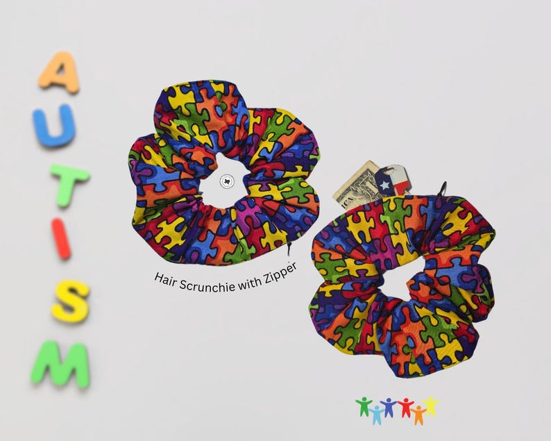 May include: Two colorful hair scrunchies with a puzzle piece pattern. The scrunchies are made of fabric and have a zipper. The text "Hair Scrunchie with Zipper" is printed below the scrunchies.