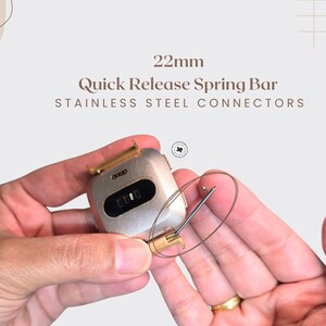 Puede incluir: Primer plano de un componente de reloj con el texto "22mm Quick Release Spring Bar Stainless Steel Connectors". El componente del reloj es plateado con un cierre dorado. Se sostiene una fina barra de resorte de metal curvada.