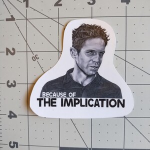 May include: A black and white sticker featuring a drawing of a man's face and the text "Because of The Implication".