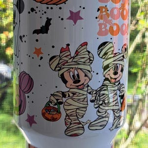Puede incluir: Vaso blanco con tem&aacute;tica de Halloween. Presenta calabazas naranjas, murci&eacute;lagos, estrellas y las palabras "Boo!" en naranja. Incluye personajes de dibujos animados disfrazados de momias. Un dise&ntilde;o festivo y divertido.