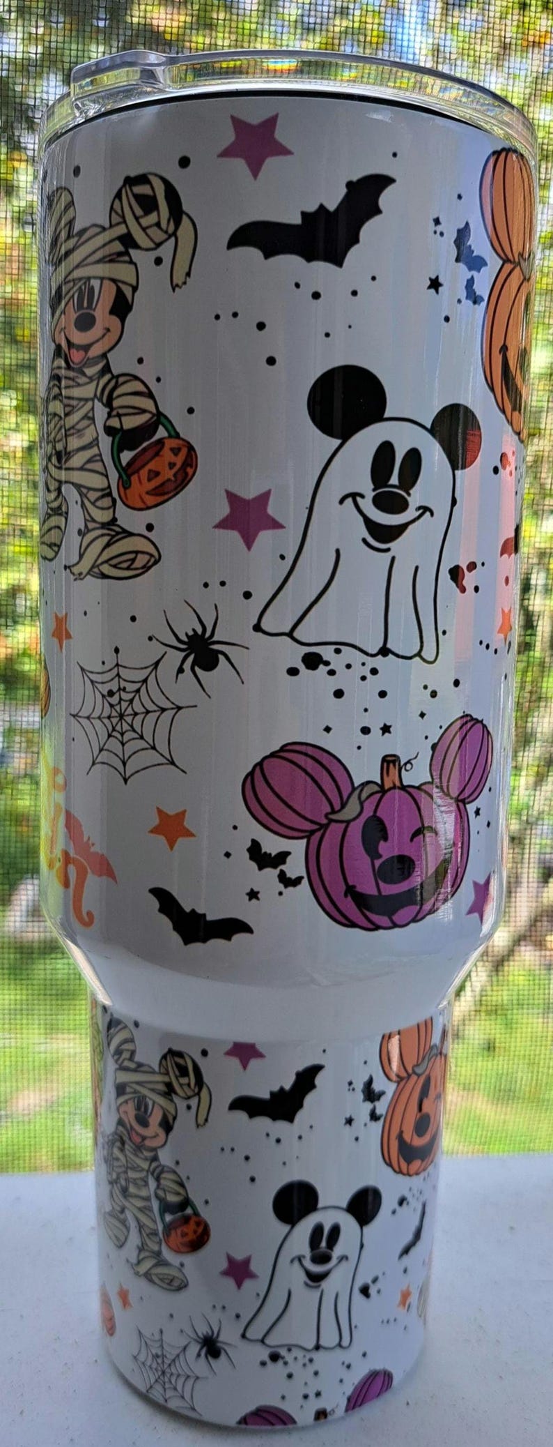 Puede incluir: Vaso blanco con un dise&ntilde;o de Halloween con personajes de dibujos animados. El dise&ntilde;o incluye una momia, un fantasma, telara&ntilde;as, murci&eacute;lagos, estrellas y calabazas con forma de Mickey Mouse. El vaso est&aacute; decorado con detalles en negro, naranja, morado y rosa.