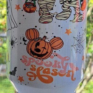 Puede incluir: Vaso blanco con gr&aacute;ficos tem&aacute;ticos de Halloween. El dise&ntilde;o incluye a Mickey y Minnie Mouse disfrazados de momias, calabazas, murci&eacute;lagos, estrellas y telara&ntilde;as. El texto "Spooky Season" tambi&eacute;n se muestra en naranja y rosa.