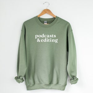 K&ouml;nnte beinhalten: Ein salbeigr&uuml;ner Pullover mit dem Text "podcasts & editing" in Wei&szlig;.