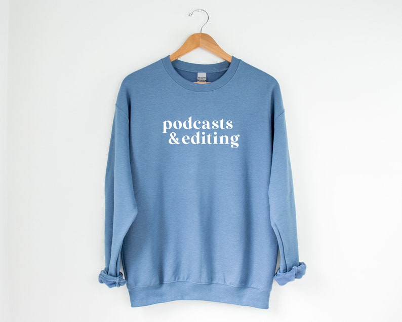 K&ouml;nnte beinhalten: Ein hellblauer Pullover mit dem Aufdruck "podcasts & editing" in Wei&szlig; auf der Vorderseite.