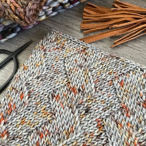 Puede incluir: Primer plano de una tela tejida con un patrón texturizado. La tela es una mezcla de hilo gris, naranja y marrón.