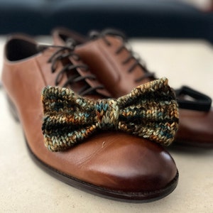 May include: A pair of brown leather shoes with a knitted bow tie on the toe of one shoe.