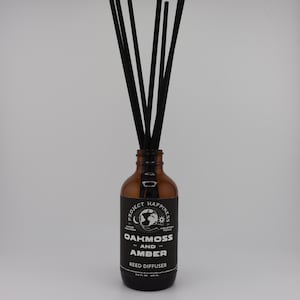 May include: A brown glass reed diffuser bottle with black reeds. The label reads "OAKMOSS AND AMBER REED DIFFUSER" with additional text. The bottle is filled with a liquid and is designed for home fragrance.