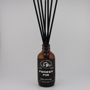 May include: A brown glass bottle with black reeds, labeled "FOREST FIR REED DIFFUSER." The label includes the text "PROJECT HAPPINESS" and a globe graphic. The reeds are arranged vertically, emanating from the bottle's opening.