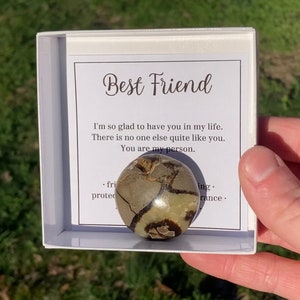 May include: A small white box with a message inside that reads "Best Friend I'm so glad to have you in my life. There is no one else quite like you. You are my person." A brown and white stone is sitting on top of the message.