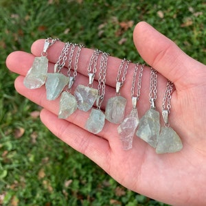 May include: A collection of ten raw aquamarine crystal pendants on silver chains. The crystals are various shades of light blue and green.