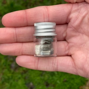 May include: A small glass jar with a silver lid filled with small grey and white stones.