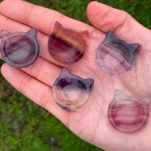 May include: Five small, colorful cat-shaped dishes made of fluorite. The dishes are purple, pink, and yellow with white streaks.