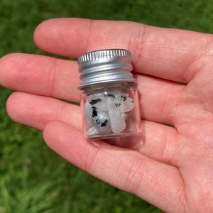 May include: A small glass jar with a silver lid filled with white and black tumbled stones.