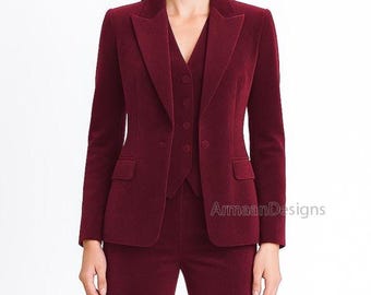 May include: A three-piece burgundy suit featuring a blazer, vest, and trousers. The blazer has a notched lapel and two front pockets. The vest has a button-down closure. The suit is made of a textured fabric and is suitable for formal occasions.