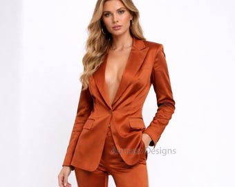 May include: A burnt orange satin suit, featuring a blazer with a single-button closure and matching trousers. The blazer has a notched lapel and pockets. The text "Armaan Designs" is visible on the right side of the image. The suit is a solid color.