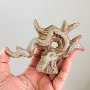 May include: A ceramic sculpture of a tree branch with a hole in the center. The sculpture is painted in shades of brown and white.