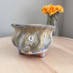 May include: A blue and yellow ceramic planter with a wavy design and three legs. The planter has a number "6" written on it.