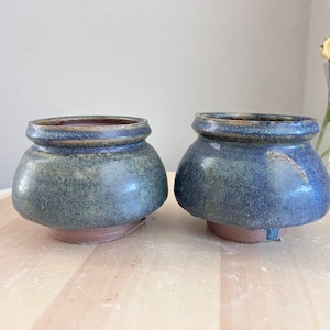May include: Two small, blue and green ceramic pots with a speckled glaze. The pots are round and have a wide opening.