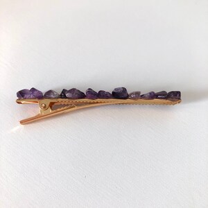 May include: A gold hair clip with a row of purple amethyst stones.