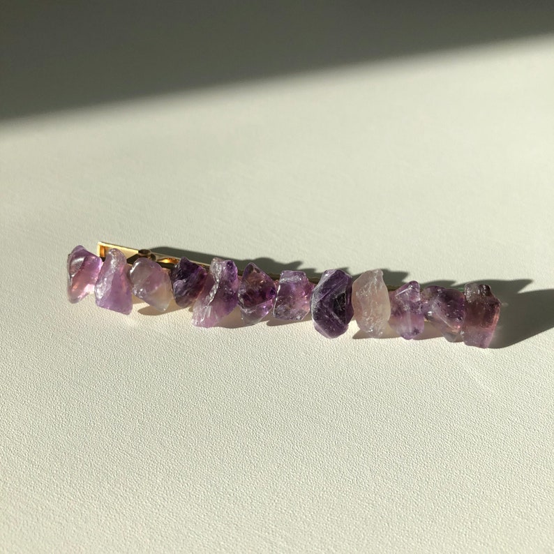 May include: A gold hair clip with a row of purple amethyst stones.
