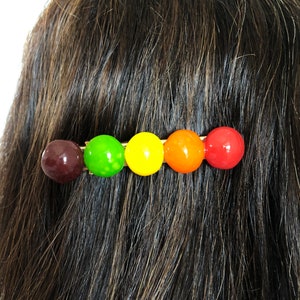 以下が含まれることがあります： 5つの丸いカラフルなビーズが付いたヘアクリップ。ビーズは茶色、緑、黄色、オレンジ、赤です。