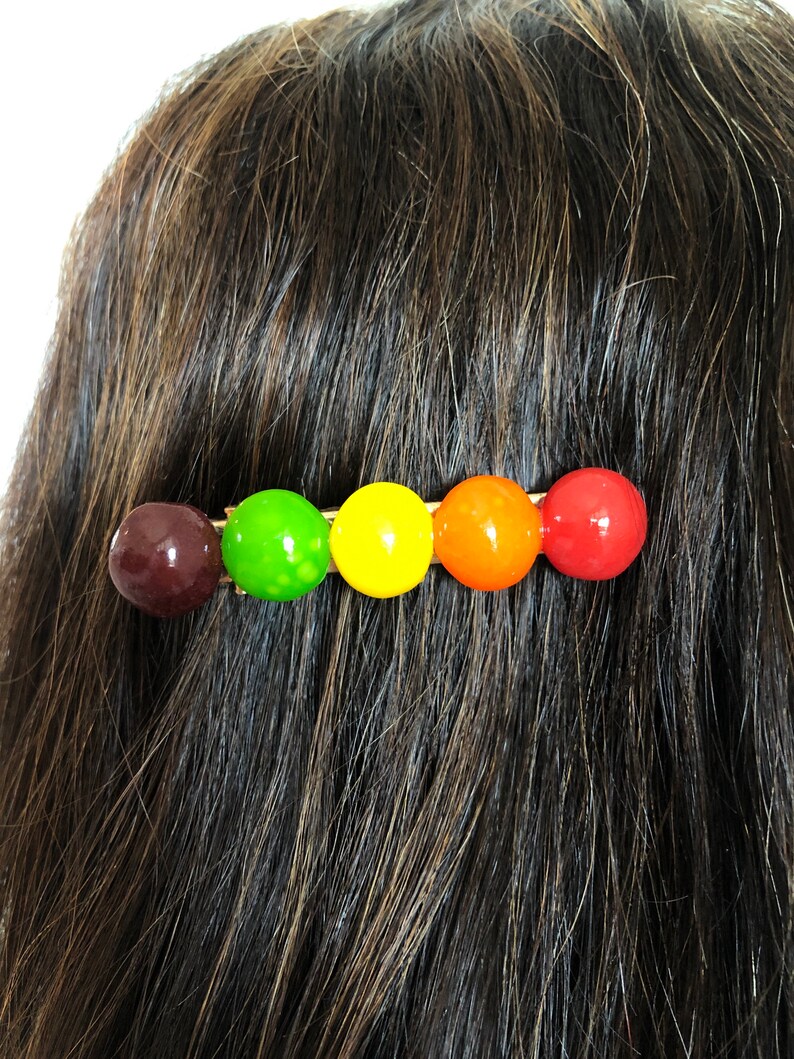 以下が含まれることがあります： 5つの丸いカラフルなビーズが付いたヘアクリップ。ビーズは茶色、緑、黄色、オレンジ、赤です。