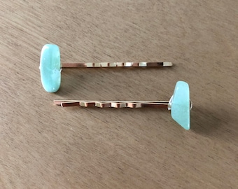 May include: Two gold hair clips with light blue glass accents. The glass accents are different shapes, one is round and the other is triangular.