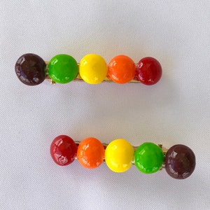 以下が含まれることがあります： 丸いカラフルなビーズが付いたヘアクリップが2セット。ビーズは茶色、緑、黄色、オレンジ、赤。クリップは金色です。