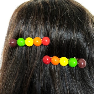 以下が含まれることがあります： カラフルな丸いビーズが並んだヘアクリップが2つ。ビーズは赤、オレンジ、黄、緑、茶色です。