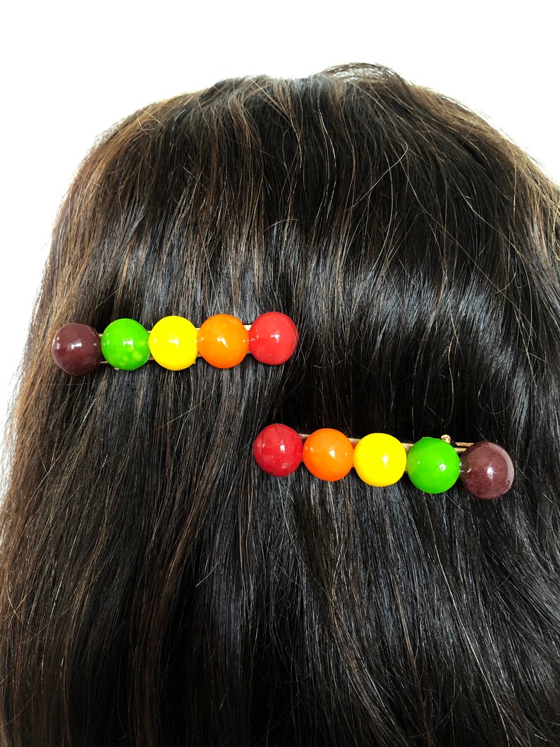 以下が含まれることがあります： カラフルな丸いビーズが並んだヘアクリップが2つ。ビーズは赤、オレンジ、黄、緑、茶色です。