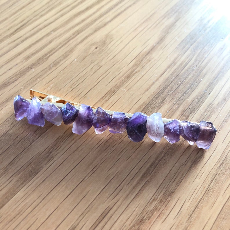 May include: A gold hair clip with a row of purple amethyst stones.