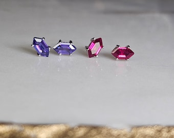 Op de afbeelding: Vier kleine oorbelletjes met edelstenen, twee zijn paars en twee zijn rood. De oorbelletjes zijn gezet in zilver.