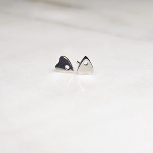 May include: A pair of silver stud earrings, one shaped like a heart and the other shaped like a triangle. Both have a small hole in the center.