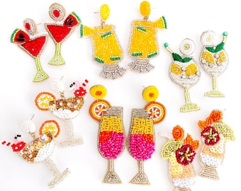 May include: A collection of beaded cocktail earrings in various designs. The earrings feature bright colors like red, yellow, and pink, with details such as watermelon slices, orange slices, and decorative embellishments. The earrings are on a white background.