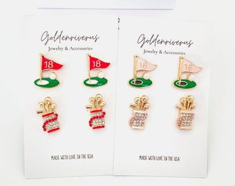 May include: Two sets of golf-themed earrings on white cards. Each set includes a golf flag with the number 18, a golf ball, and a golf bag with golf clubs. The earrings are gold-toned with red, green, and pink accents. The text "MADE WITH LOVE IN THE USA" is printed on the cards.