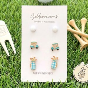 May include: Three pairs of stud earrings on a white display card labeled Goldenriverus Jewelry & Accessories. The earrings feature white golf ball designs, light blue and gold golf carts, and light blue checkered golf bags with gold accents.