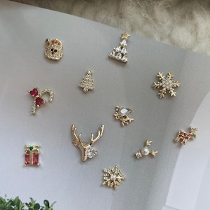 Pode incluir: Conjunto de pingentes para unhas com tema natalino em tom dourado. Os pingentes incluem um boneco de neve, uma &aacute;rvore de Natal, um bast&atilde;o de caramelo, uma rena, um floco de neve, uma caixa de presente e uma estrela.